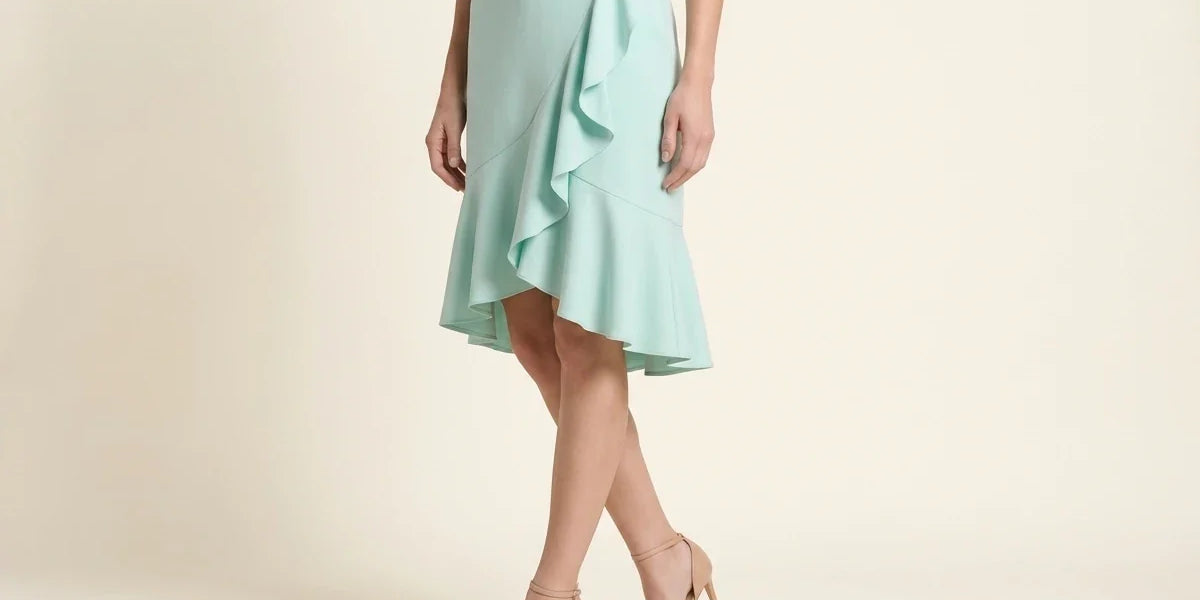 Cropped view of a woman wearing a light mint green ruffled midi skirt, black top, and nude pointed-toe ankle-strap pumps against a neutral studio backdrop.