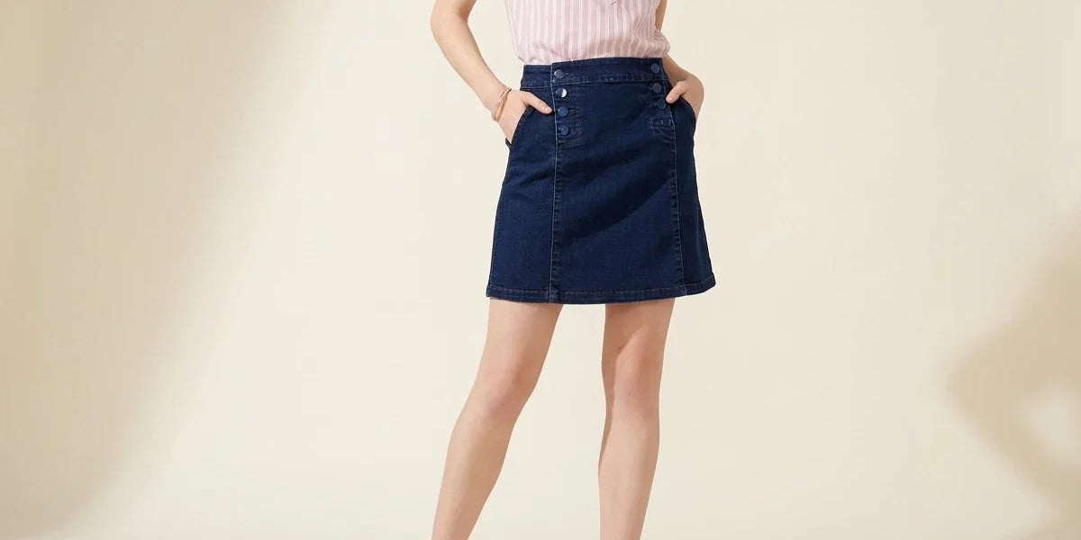 Cropped view of a woman wearing a Charter Club dark wash denim A-line mini skirt with sailor-button pocket details, a pink striped blouse, and tan ballet flats.