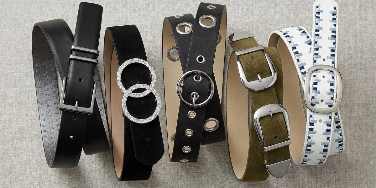 Flat lay of five assorted fashion belts featuring leather, suede, rhinestone, grommet, and patterned styles on a neutral linen background.