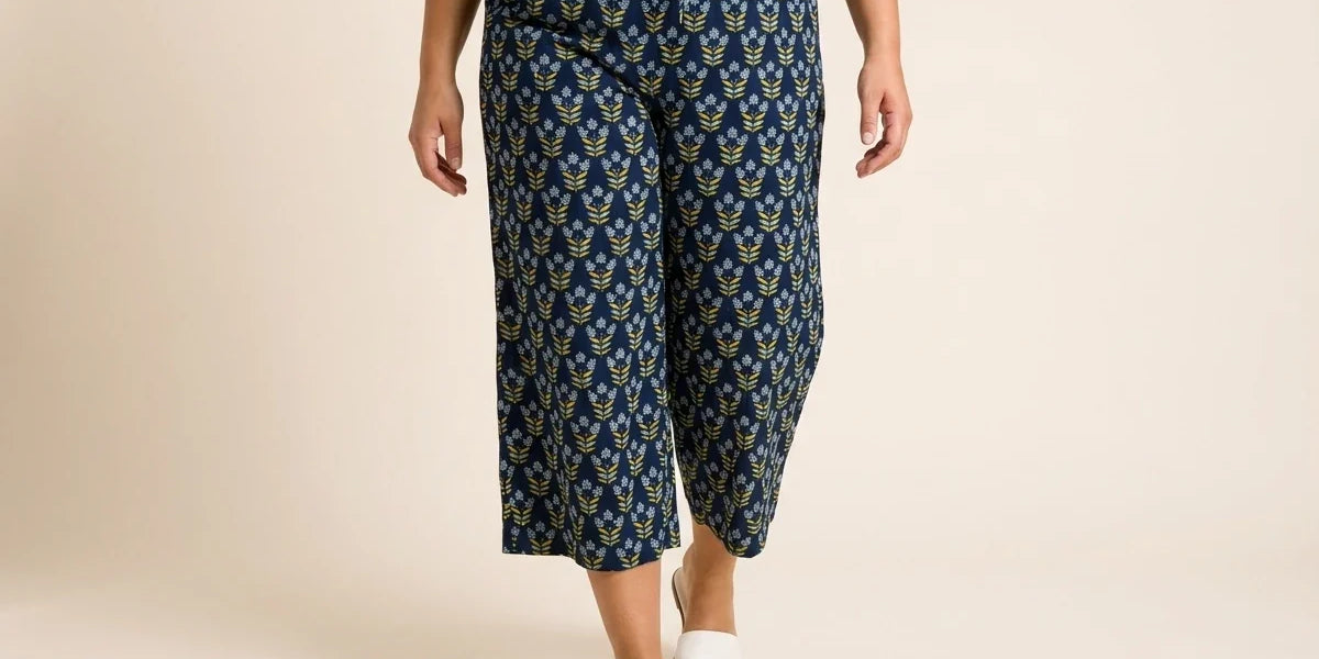 Cropped view of a woman wearing navy blue floral print wide-leg culotte pants with a drawstring waist and white slide sandals.