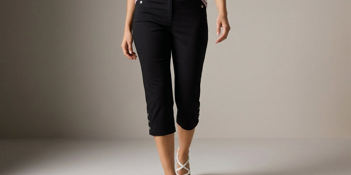 A model wearing black cropped capri pants, a striped short-sleeve top, and white strappy high-heeled sandals, walking against a neutral studio background.