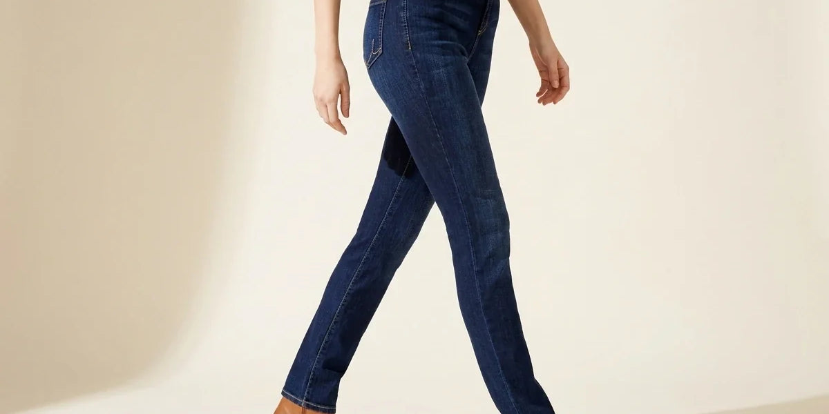 Cropped view of a woman walking in dark-wash slim straight jeans paired with tan leather ankle boots.