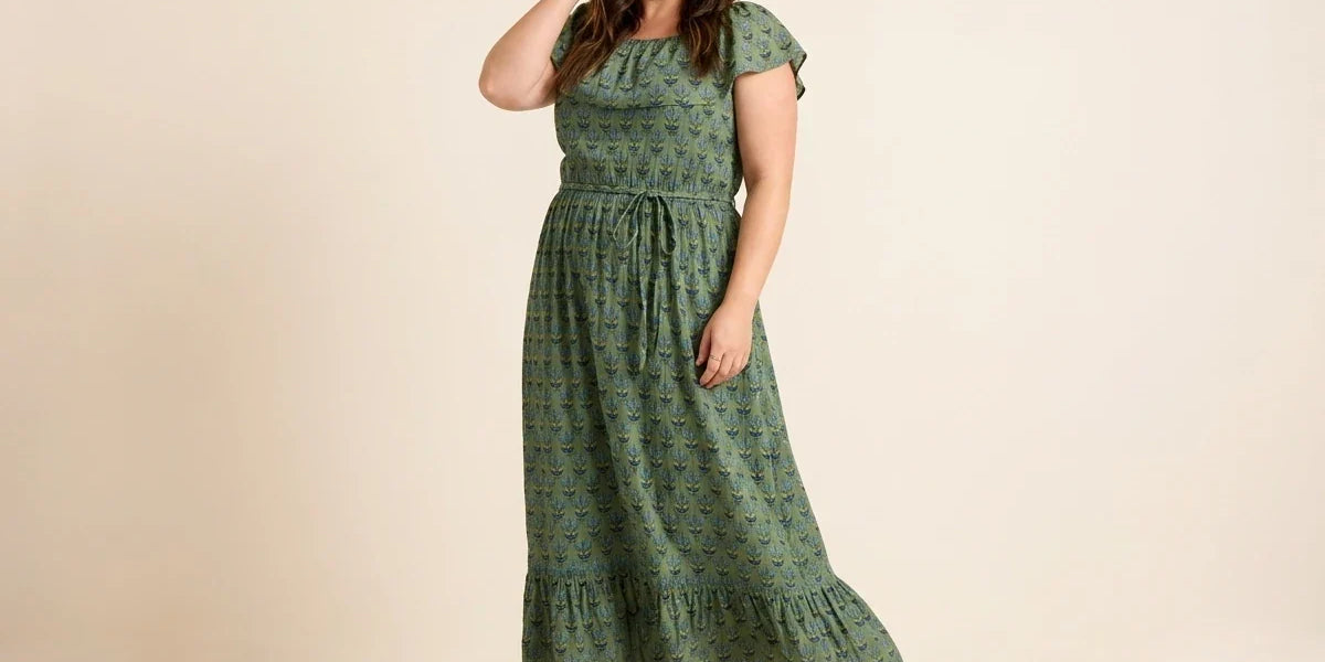 Brunette woman modeling a plus-size olive green floral maxi dress with flutter sleeves, a tie waist, and tan block heel sandals.
