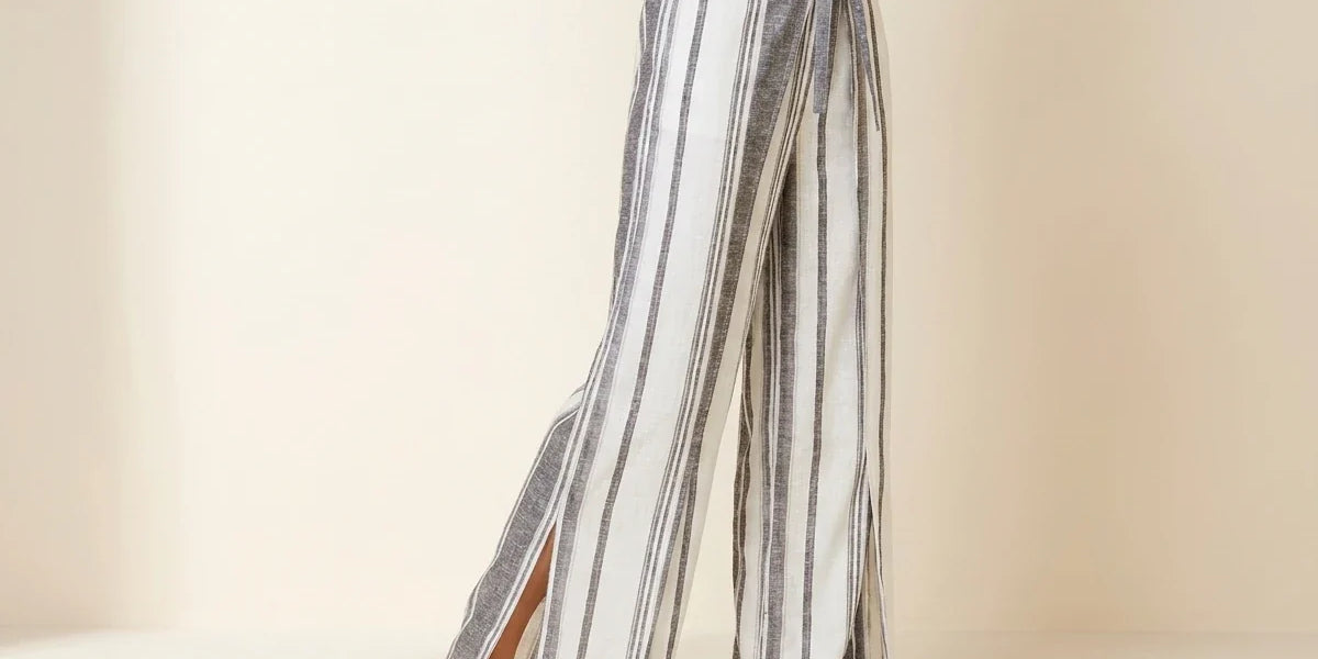 Cropped view of a woman wearing black and cream striped wide-leg linen pants with high side slits and nude leather slide sandals.