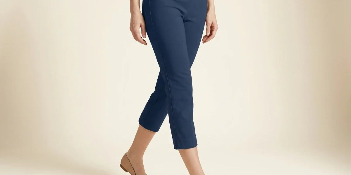 Cropped view of a woman wearing petite navy blue slim-fit cropped ankle pants paired with nude pointed-toe flat shoes.