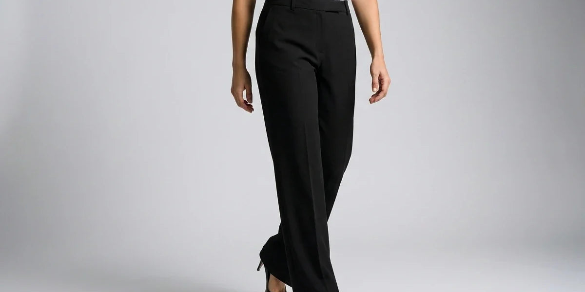 A model wearing black wide-leg trousers, styled with a white short-sleeve top and black pointed-toe heels, shown from the waist down against a light gray studio background.