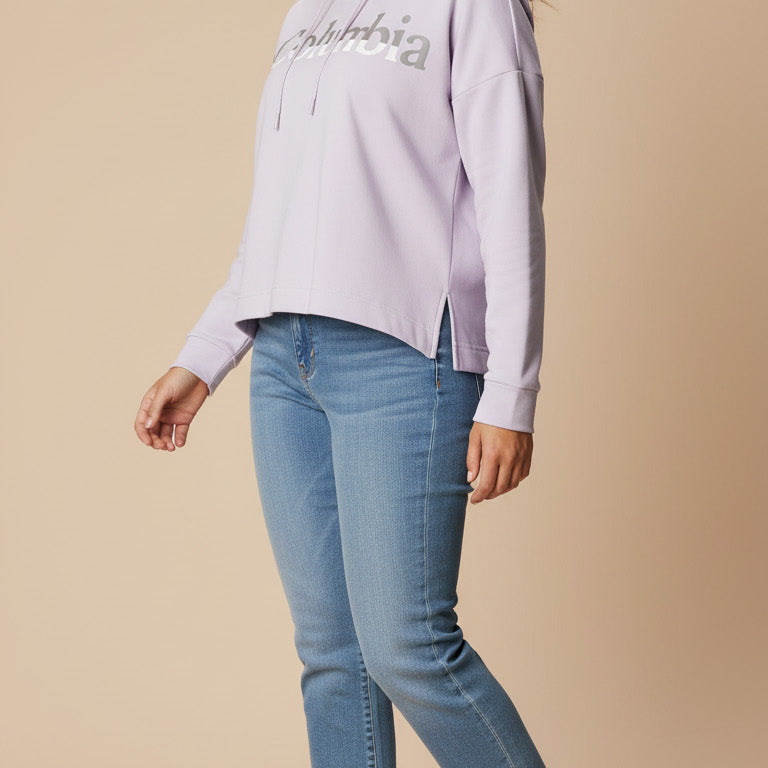 Woman wearing a light purple hoodie with text and blue jeans on a beige background