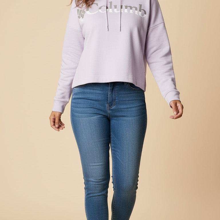 Woman wearing a light purple hoodie with text and blue jeans on a beige background