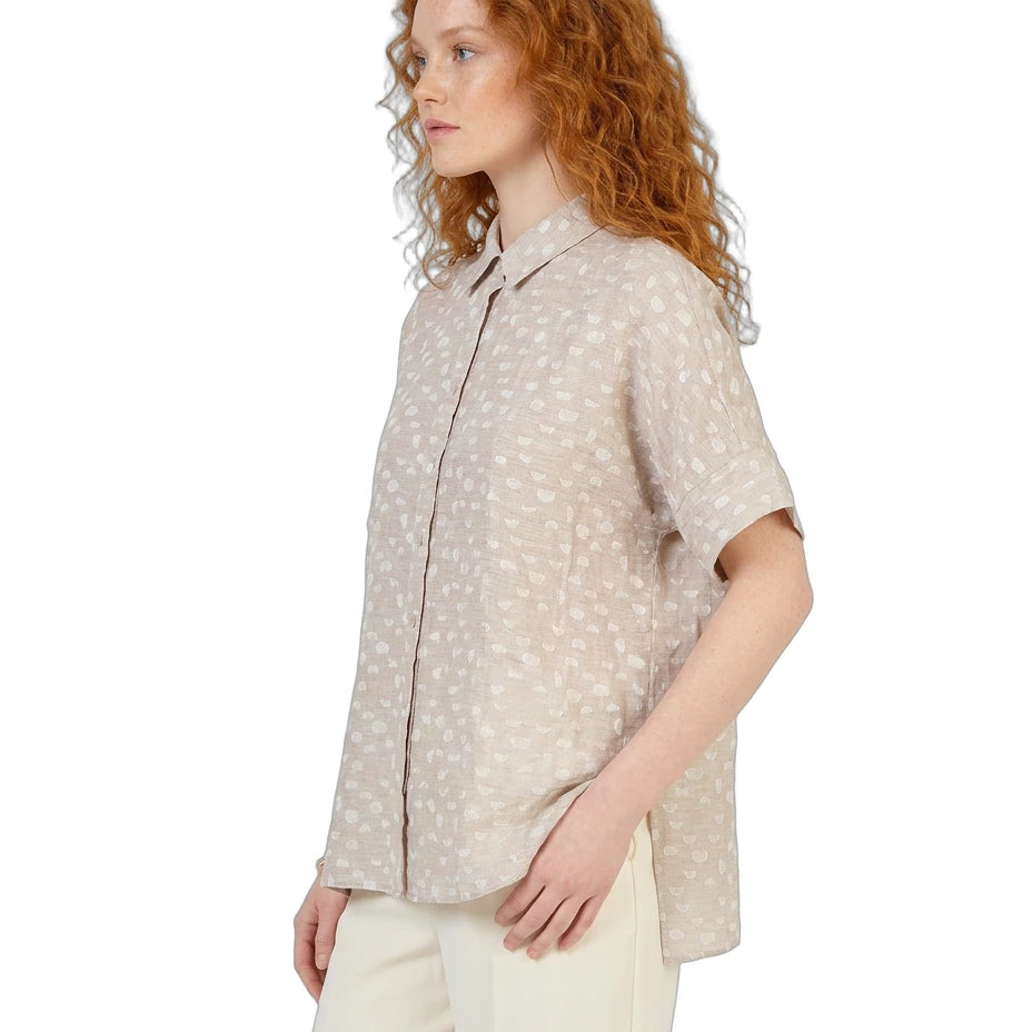 Woman wearing a beige patterned shirt and white pants on a white background