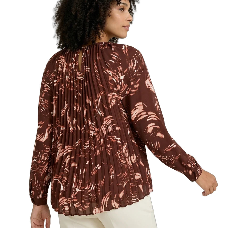 Woman wearing a brown patterned blouse with white pants on a white background