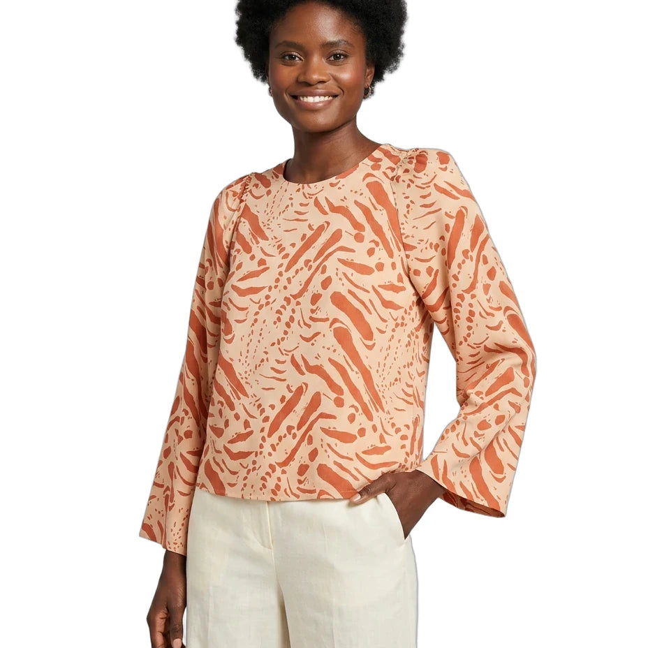 Woman wearing a patterned orange and beige top with white pants on a white background