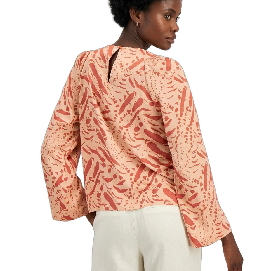 Woman wearing a patterned peach blouse and white pants on a white background