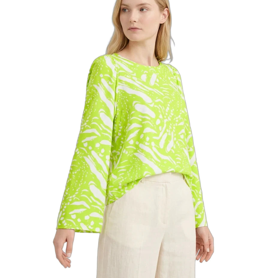 Woman wearing a bright green patterned top and beige pants on a white background