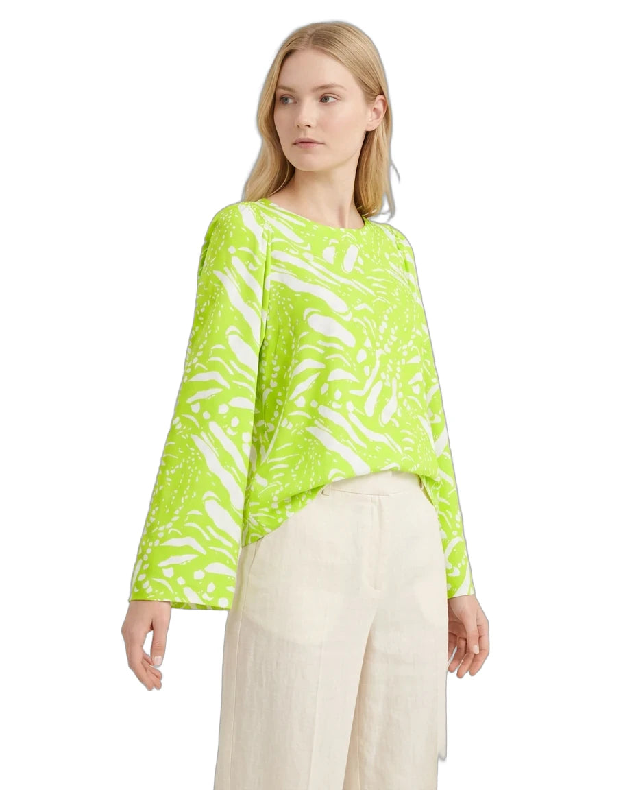Woman wearing a bright green patterned top and beige pants on a white background