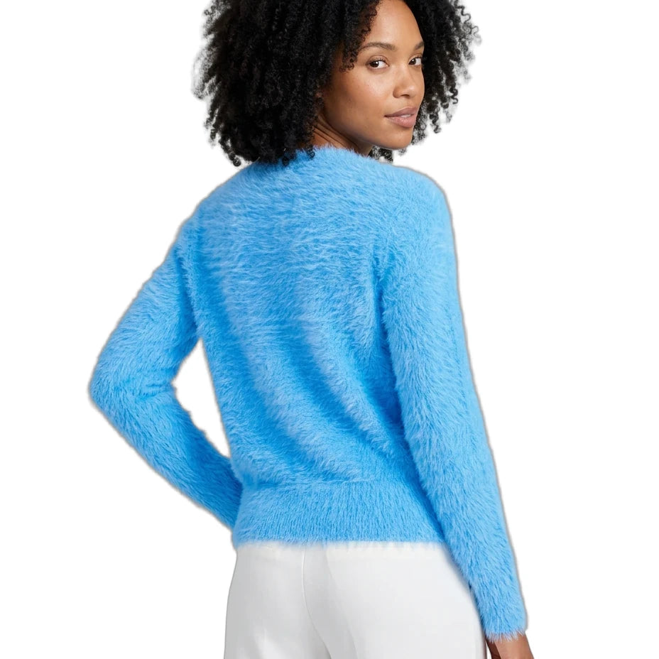 A woman with curly black hair is shown from the back wearing a fuzzy, textured light blue long-sleeve sweater and white pants against a plain white background.