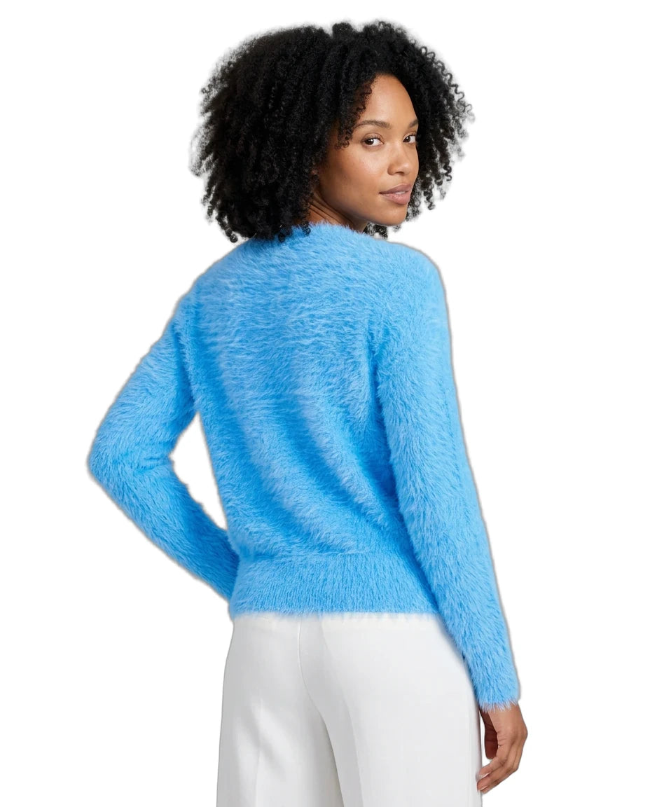 A woman with curly black hair is shown from the back wearing a fuzzy, textured light blue long-sleeve sweater and white pants against a plain white background.
