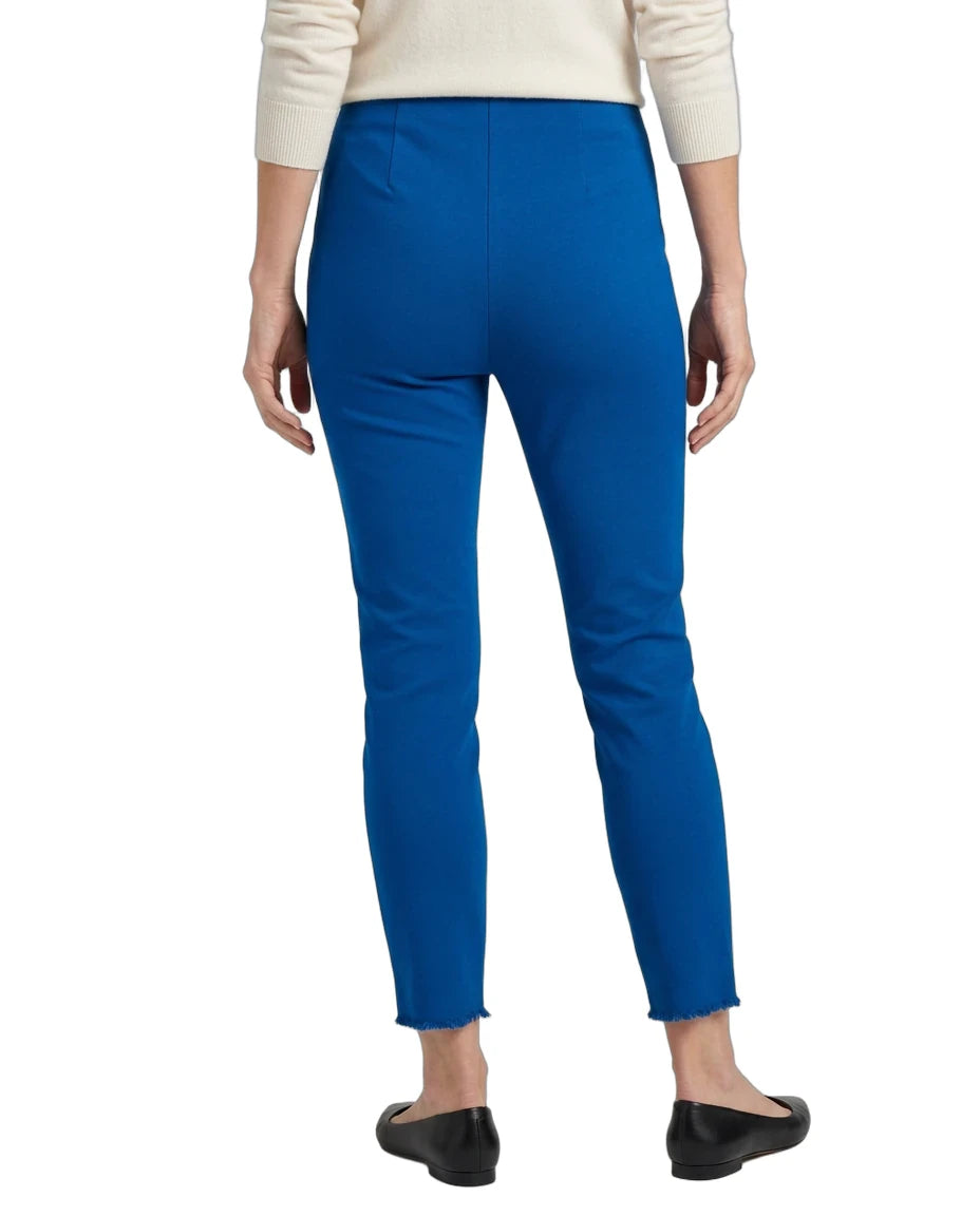 A person shown from the back wearing bright royal blue cropped pants, a cream long-sleeve top, and black flats against a plain white studio background.