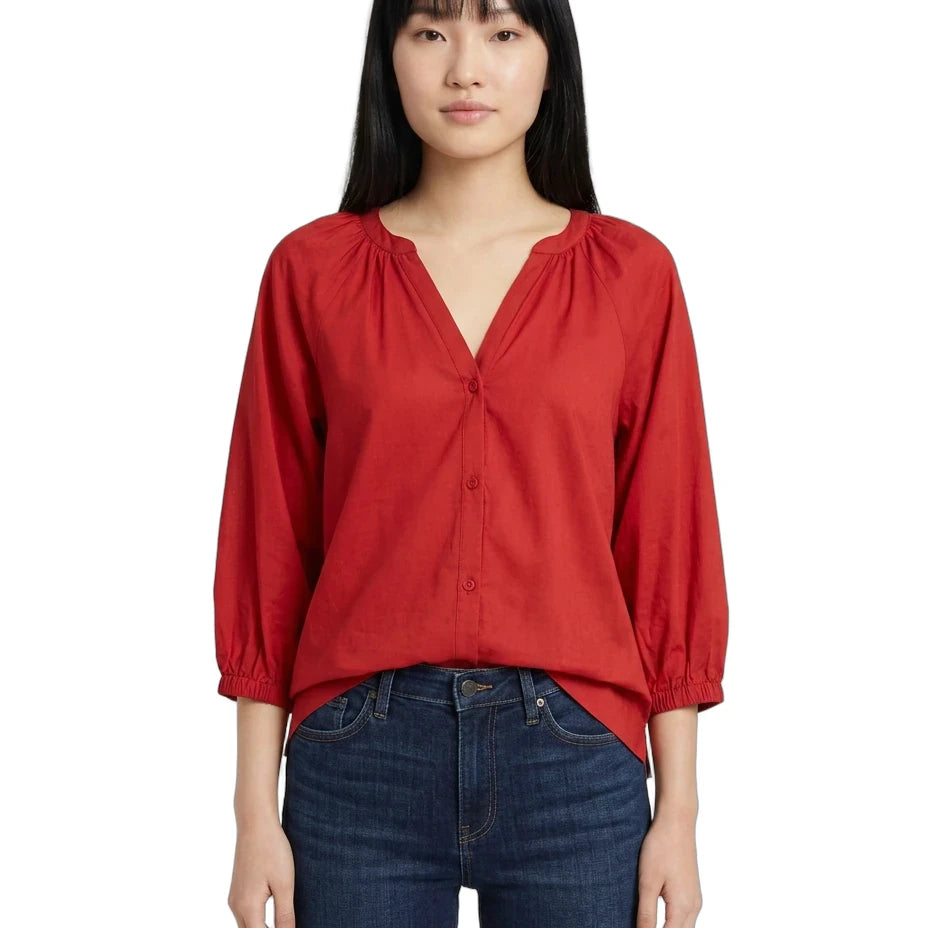 A woman modeling a red long-sleeve blouse with a gathered V-neckline and button front, paired with dark blue jeans, against a plain white background.