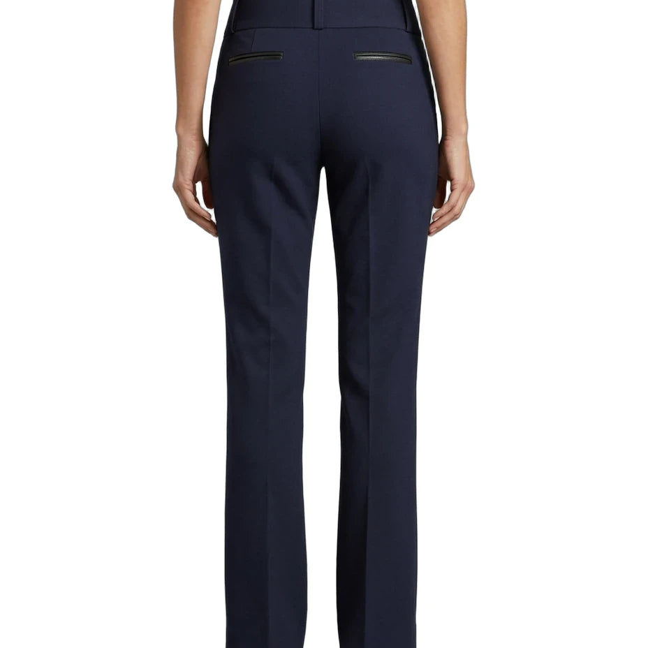 A person shown from the back wearing navy blue straight-leg trousers with zippered back pockets, paired with a light top and brown shoes, against a plain white background.