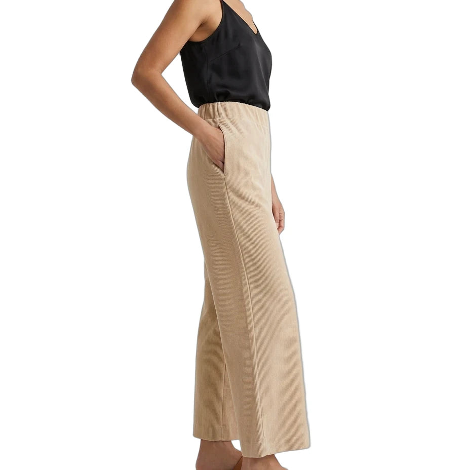 A woman shown in side profile wearing a black camisole top and beige wide-leg pants with side pockets, paired with tan slide sandals, against a plain white background.
