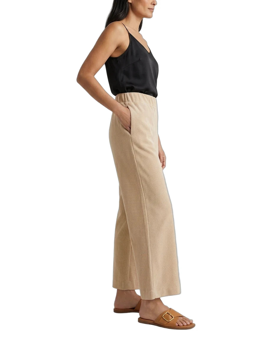 A woman shown in side profile wearing a black camisole top and beige wide-leg pants with side pockets, paired with tan slide sandals, against a plain white background.