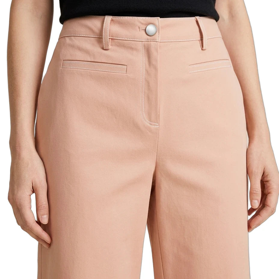 A close-up of a model wearing high-waisted peach-colored wide-leg trousers with belt loops, a silver button, and welt pockets, paired with a black top.