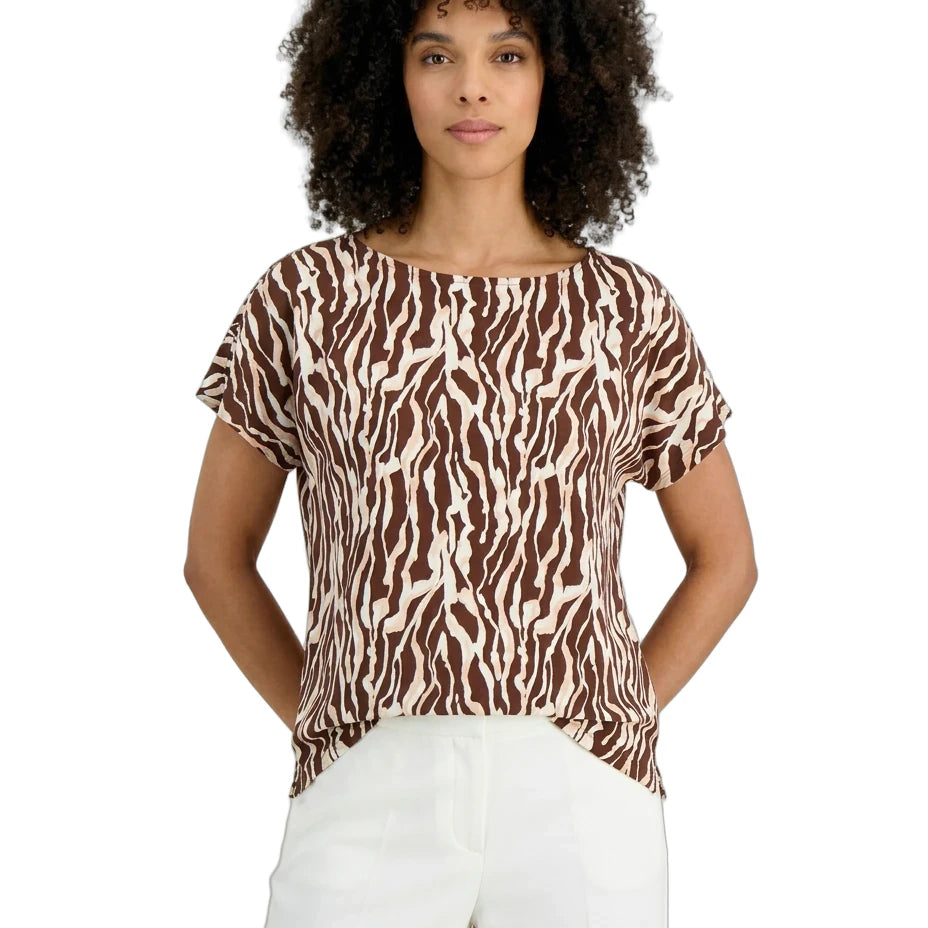 Woman wearing a brown and white patterned top with white pants on a white background