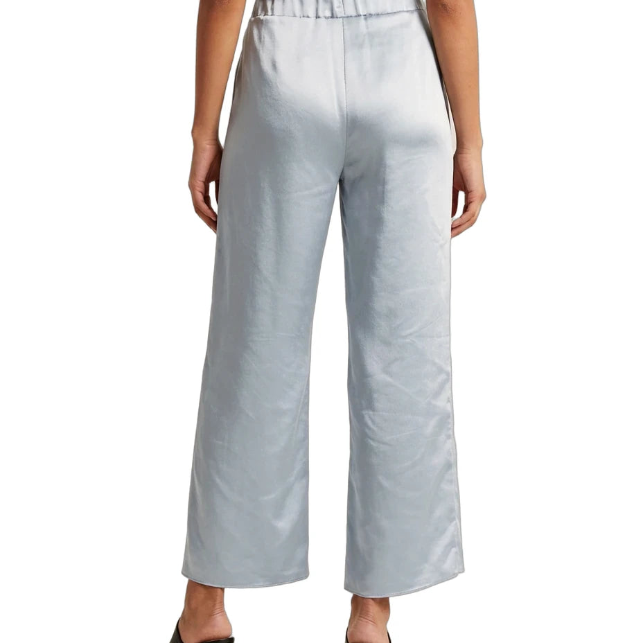 A model from the back wearing light blue wide-leg cropped trousers with a satin-like sheen, paired with a black top and black block-heel mules, against a plain white background.