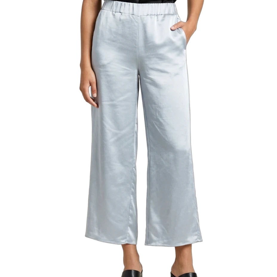 A model wearing light silver wide-leg cropped pants with an elastic waistband, styled with a black satin top and black leather mule shoes against a plain white background.