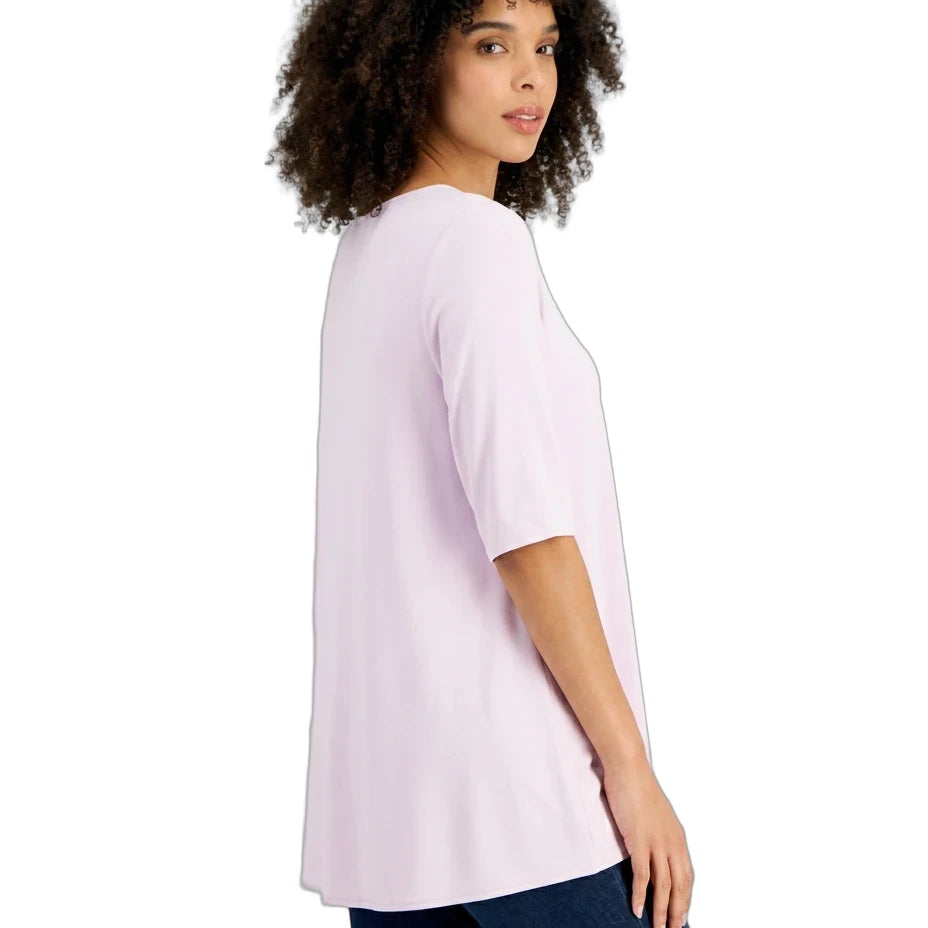 A woman with curly dark hair is shown from the side/back wearing a light pink short-sleeve tunic top and dark blue jeans against a plain white background.