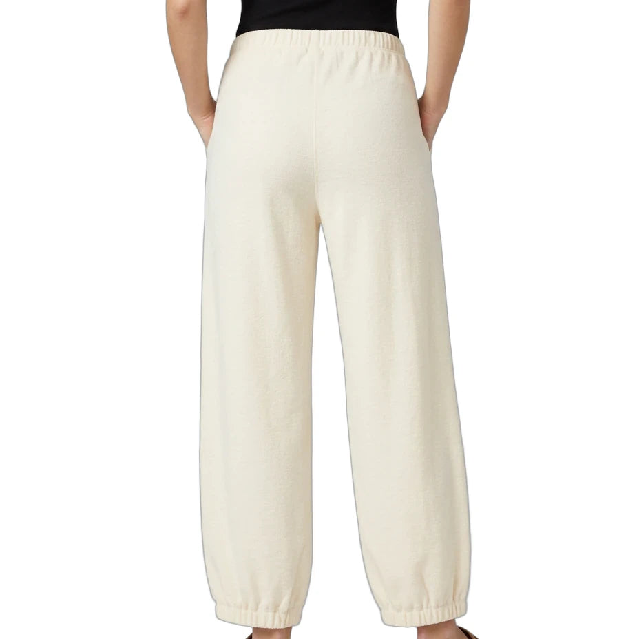A person shown from the back wearing cream-colored wide-leg lounge pants, a black sleeveless top, and tan slip-on shoes against a plain white background.