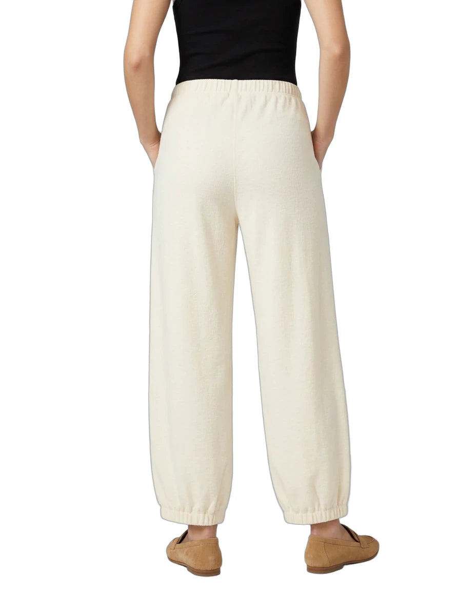 A person shown from the back wearing cream-colored wide-leg lounge pants, a black sleeveless top, and tan slip-on shoes against a plain white background.