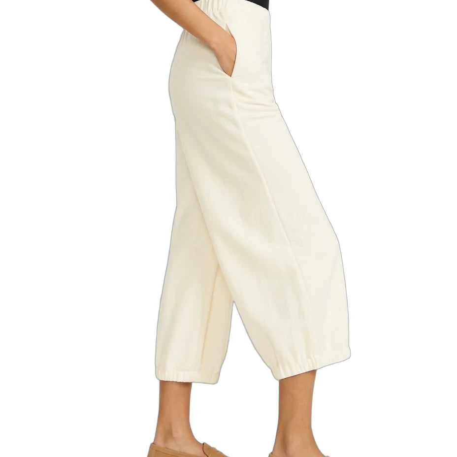 A person wearing off-white cropped wide-leg pants with side pockets, paired with a black top and tan loafers, shown against a plain white background.