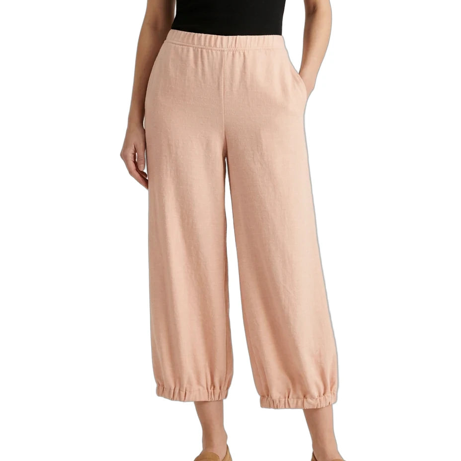 A model wearing light peach wide-leg cropped pants with an elastic waistband and gathered cuffs, paired with a black top and tan loafers, shown against a plain white background.