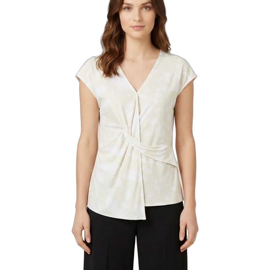 A woman modeling a cream-colored wrap-style blouse with cap sleeves and a twisted front detail, paired with black pants, against a plain white background.