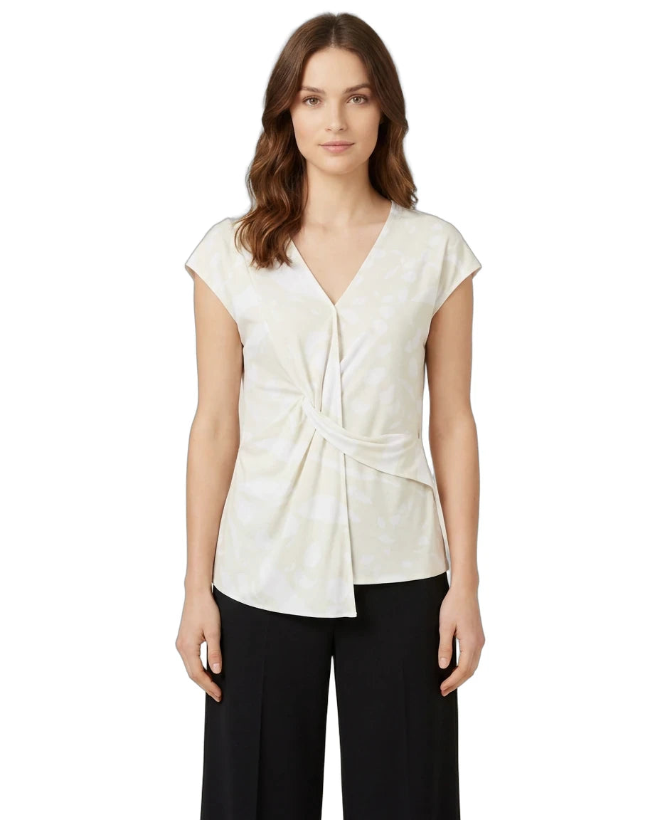 A woman modeling a cream-colored wrap-style blouse with cap sleeves and a twisted front detail, paired with black pants, against a plain white background.