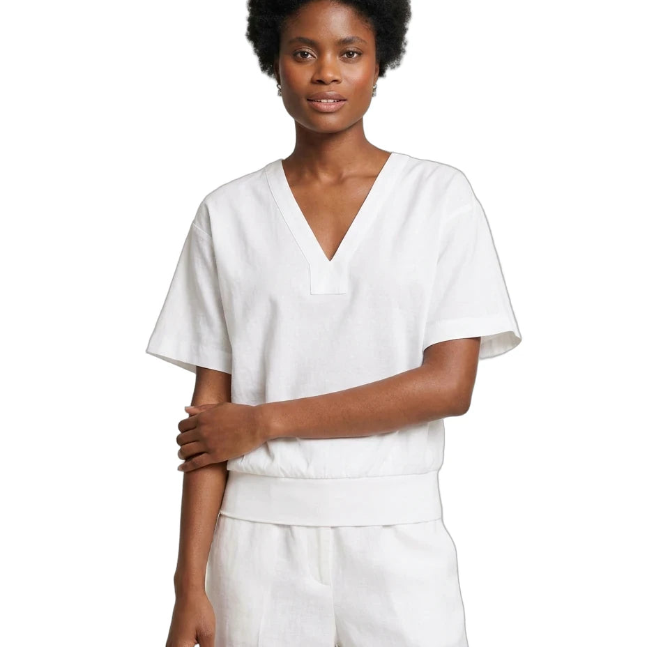A woman modeling a white short-sleeve V-neck scrub top with matching white pants against a plain white background.