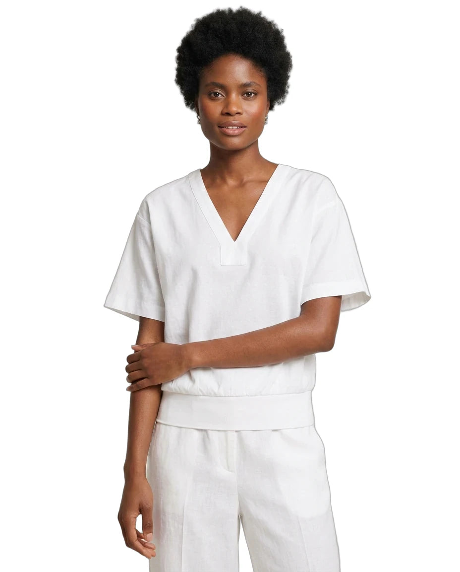 A woman modeling a white short-sleeve V-neck scrub top with matching white pants against a plain white background.