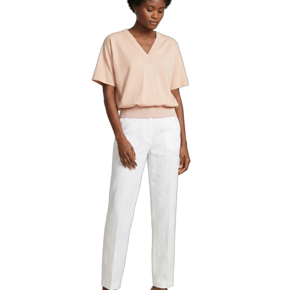 A model wearing a light peach V-neck short-sleeve top and white straight-leg trousers, paired with black heeled mule sandals, against a plain white background.