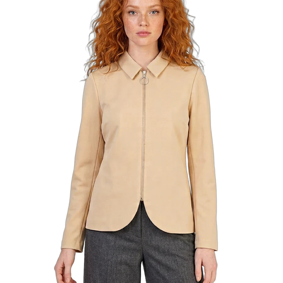 A model with curly red hair wearing a beige zip-up collared jacket and dark gray trousers, photographed against a solid white background.