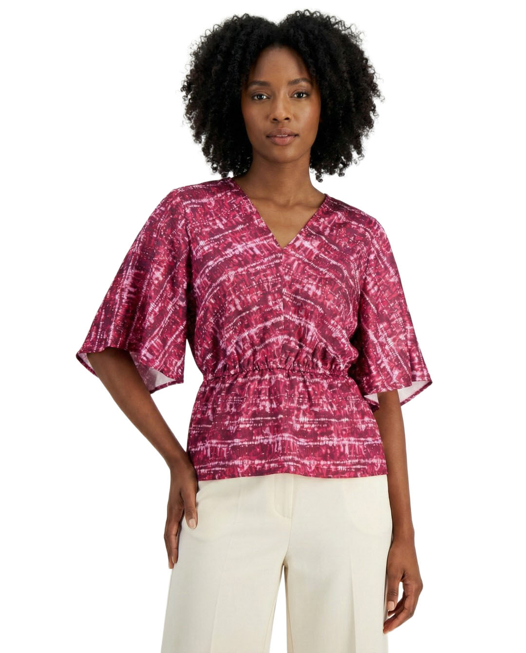 Woman wearing a pink patterned top and white pants on a white background