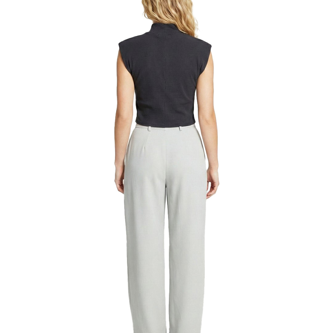Woman wearing a black sleeveless top and light gray pants on a white background