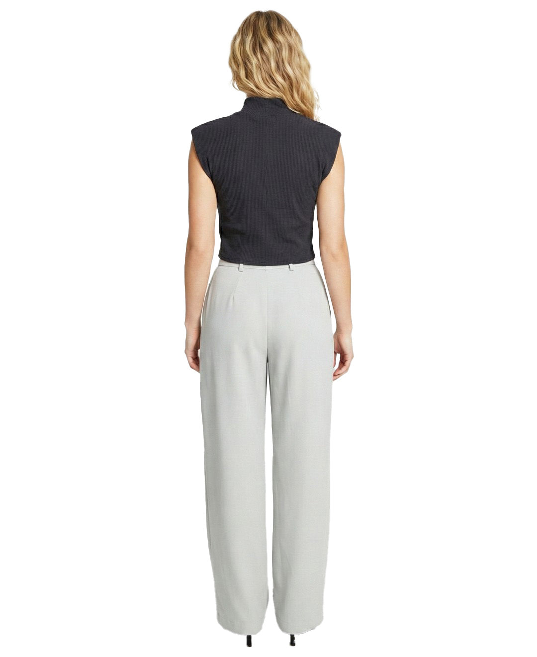 Woman wearing a black sleeveless top and light gray pants on a white background