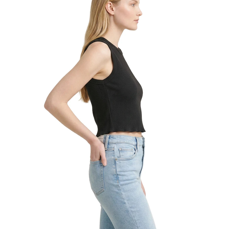 Woman wearing a black sleeveless top and light blue jeans on a white background