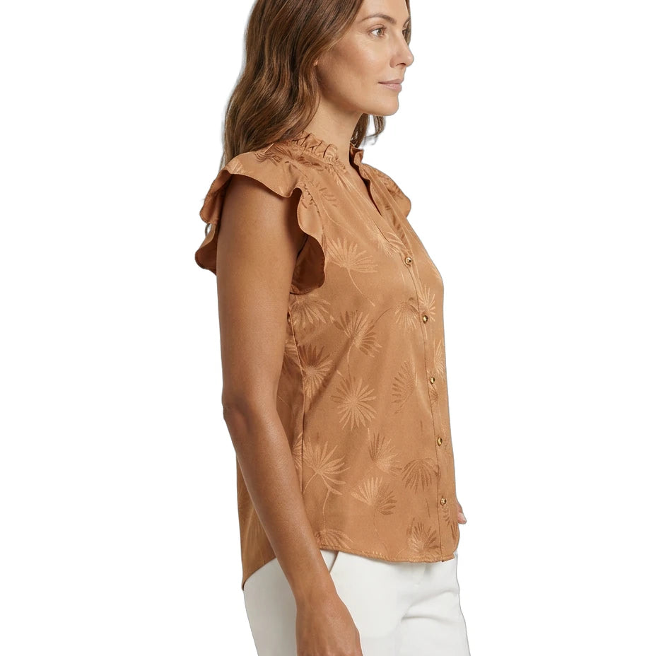 Woman wearing a brown floral Calvin Klein blouse with white pants on a white background