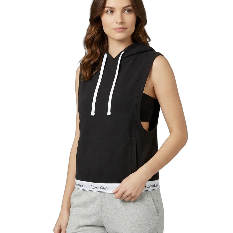 Woman wearing a Calvin Klein black sleeveless hoodie with cut-out design and gray sweatpants on a white background