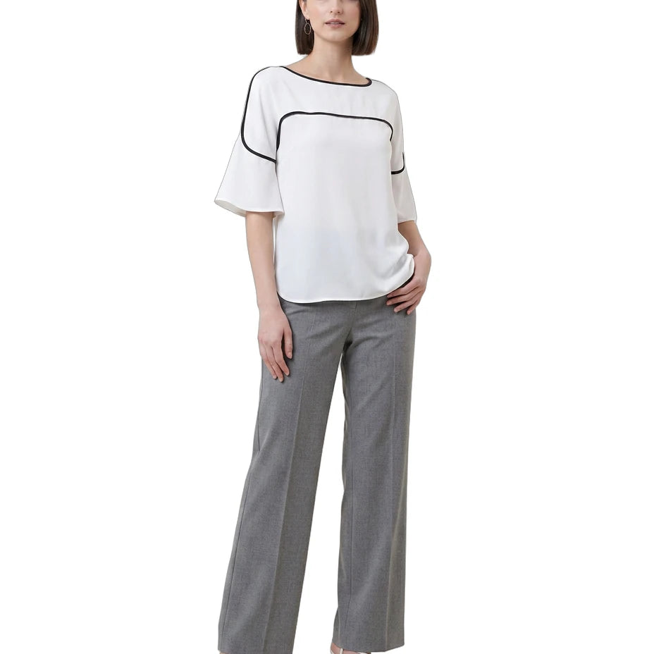 Woman wearing a white Calvin Klein blouse with black trim and gray pants on a white background