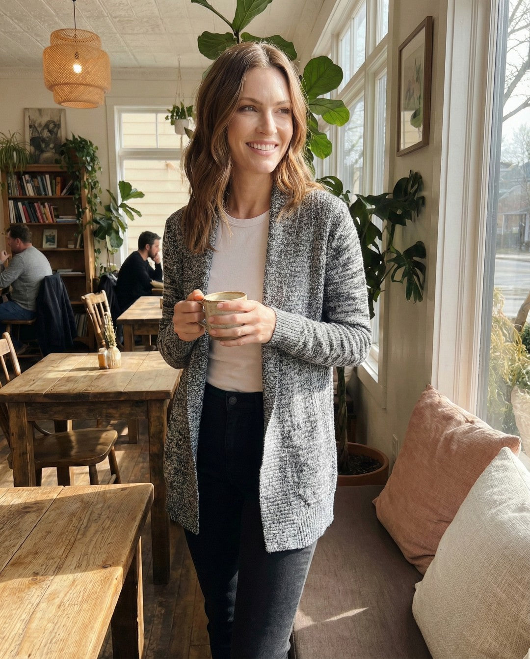 Woman holding a cup in a cozy cafe with wooden tables and plants.