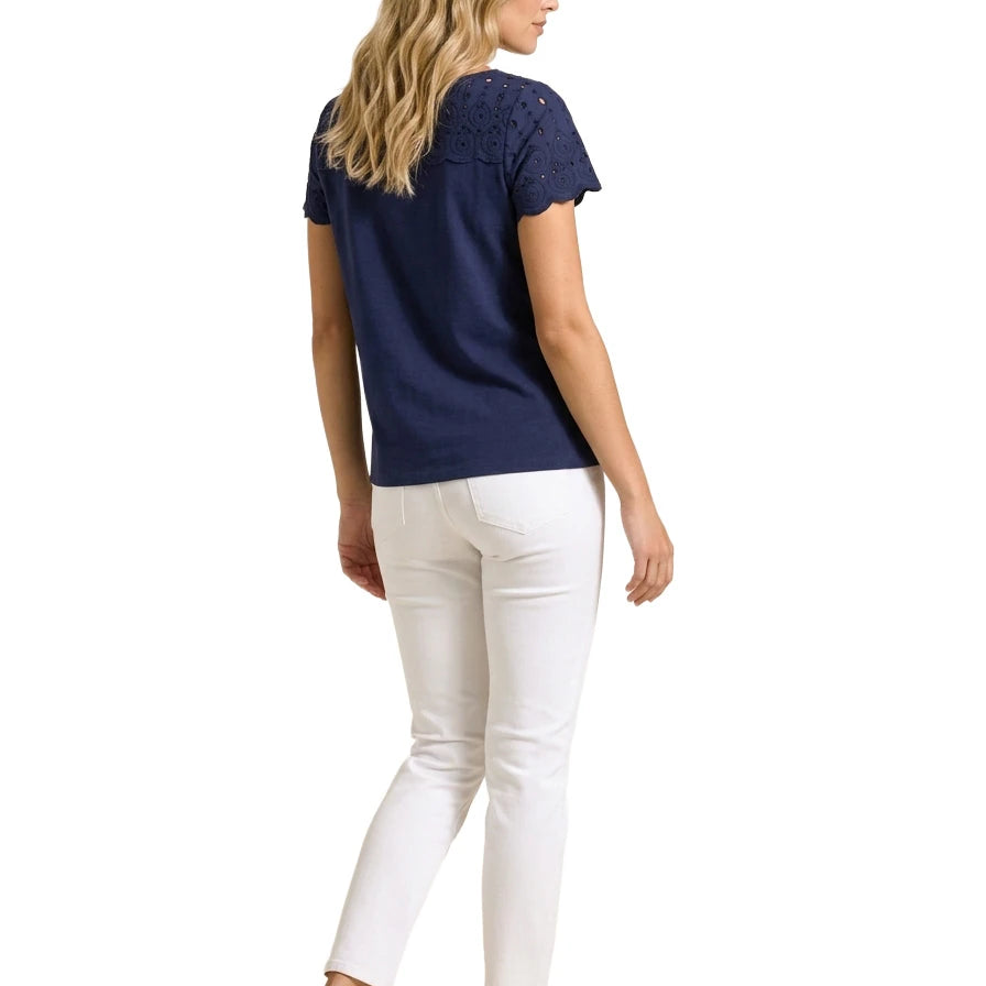 Full-length rear view of a woman wearing a navy blue short-sleeve eyelet top, white straight-leg jeans, and navy driving loafers.