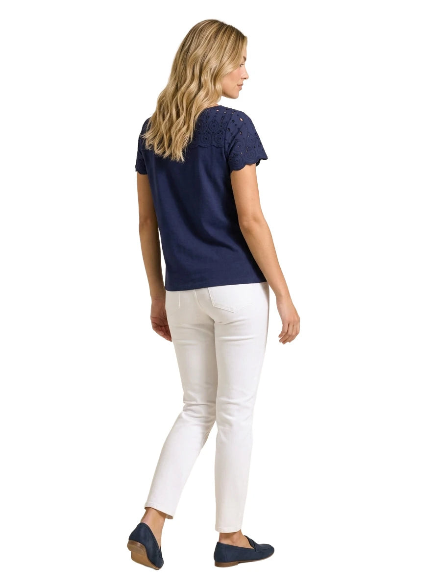 Full-length rear view of a woman wearing a navy blue short-sleeve eyelet top, white straight-leg jeans, and navy driving loafers.